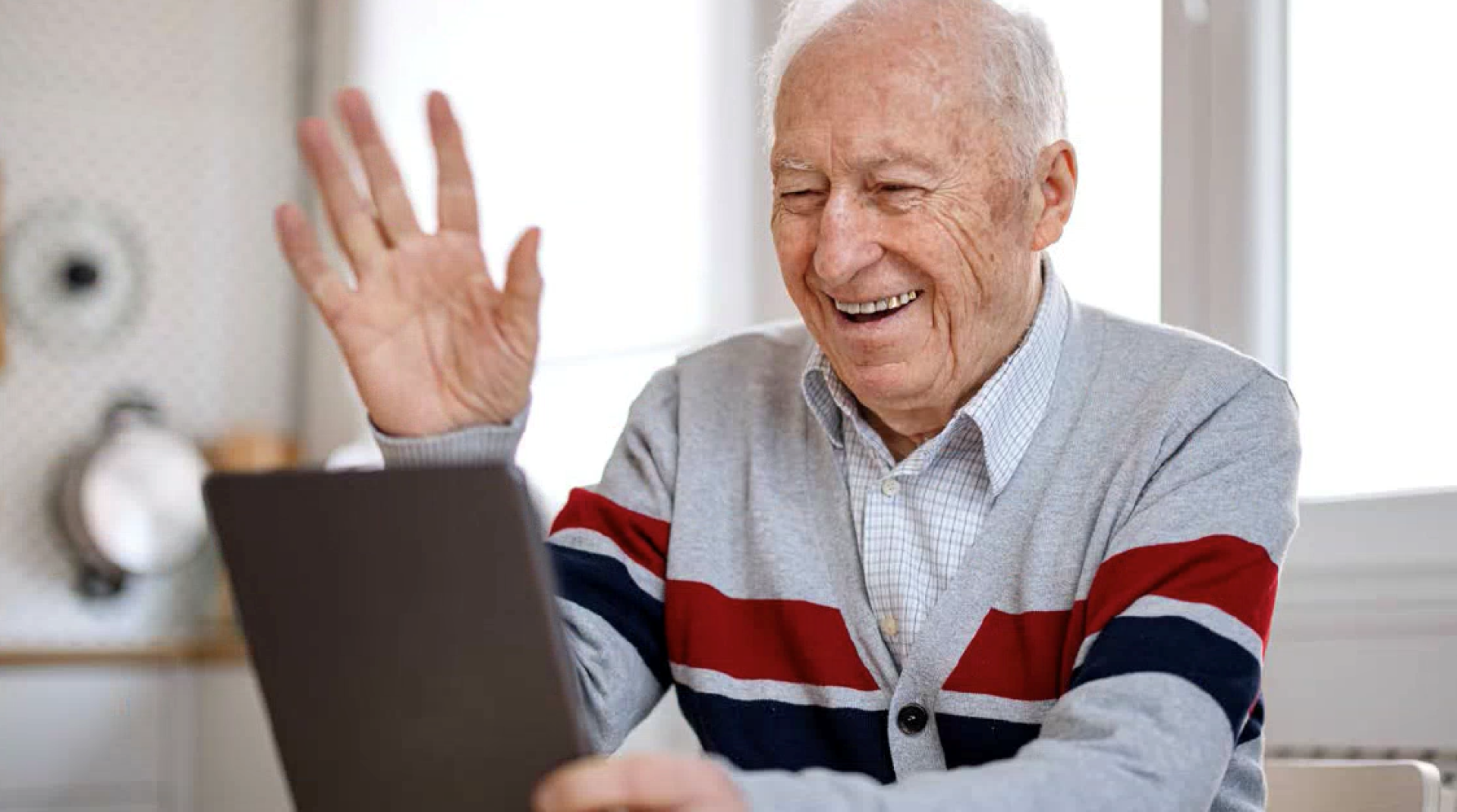 Older man smiling and waving to somebody via tablet device.